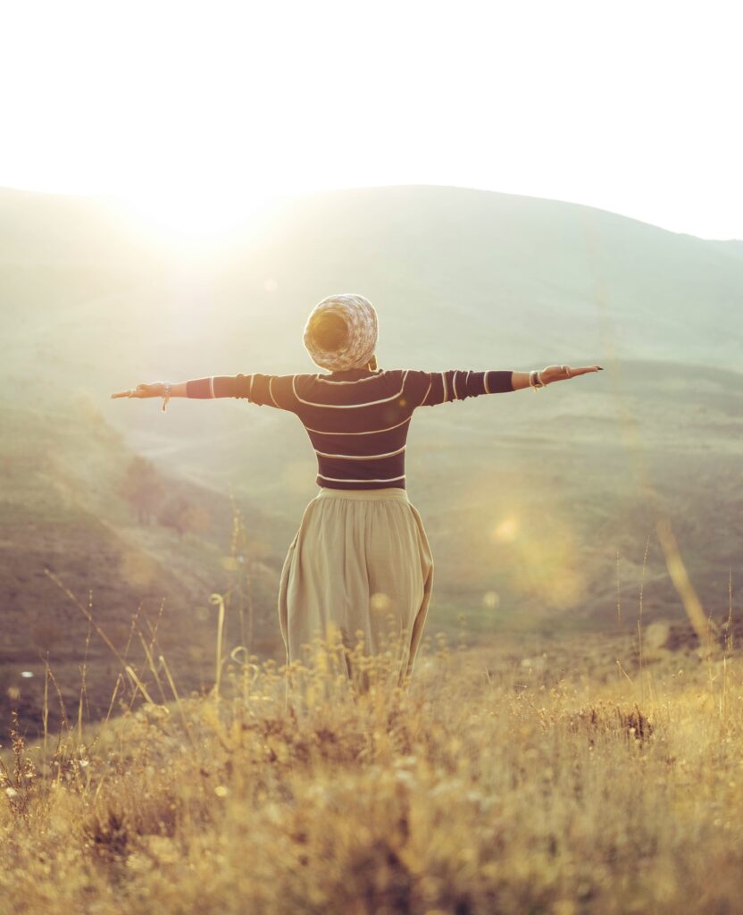 Mulher de braços abertos em paisagem natural ensolarada representando liberdade e saúde mental.